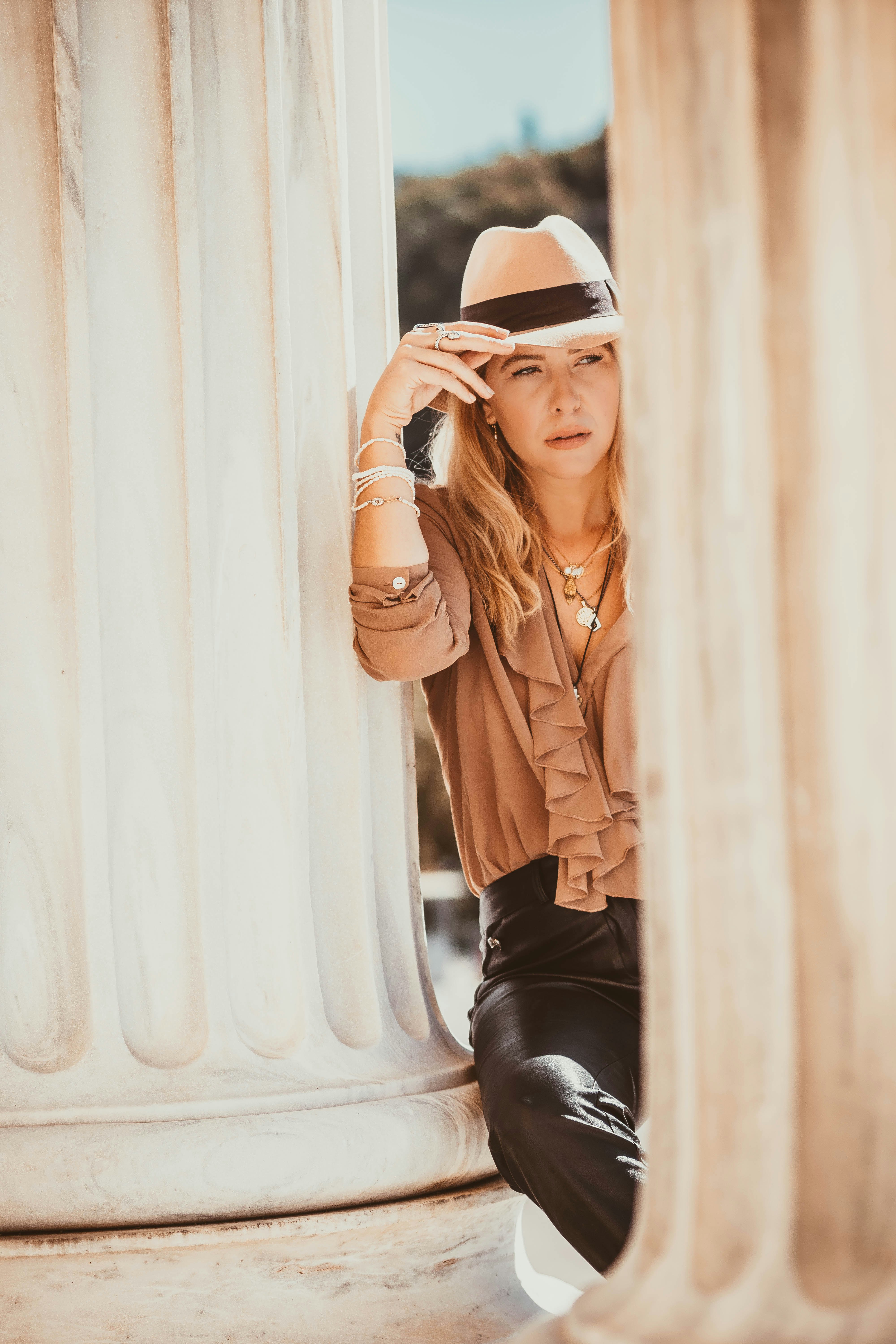 woman in brown leather jacket and black pants sitting on white concrete wall